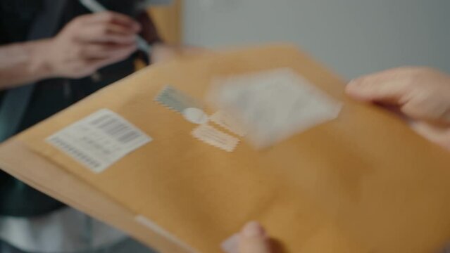 Hands of female recipient signing proof of delivery form, taking mail from courier and checking envelopes. Close-up shot