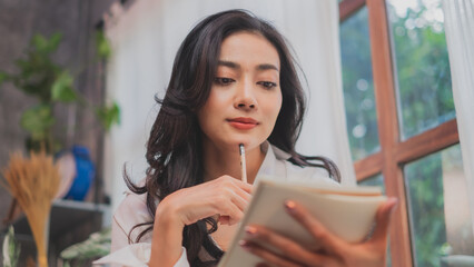 An Asian woman is looking at notebook while thinking. concept of artist having an inspiration or an idea for art work or architect planning for work. Confidence woman.  advertise