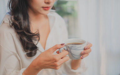 Hand holding a cup of coffee in the morning with cozy, warm, freedom, relaxing atmosphere. Concept of weekend break time, inspiration time, wellness daytime.