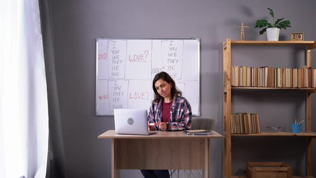 Learning English online. Attractive female teacher giving foreign language lesson on internet using laptop computer, explaining grammar rules to students on web.