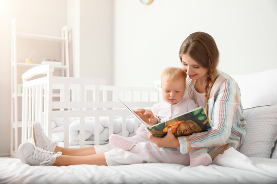 Young mother reading book to her cute little baby on bed
