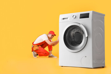 Young plumber with washing machine on yellow background