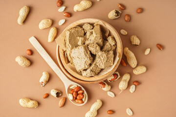 Wooden bowl of sweet halva and peanuts on color background
