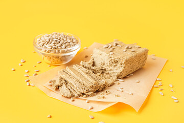 Sheet of baking paper with tasty halva and sunflower seeds on yellow background