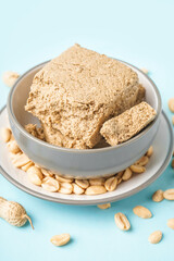 Bowl of tasty halva and peanuts on color background, closeup