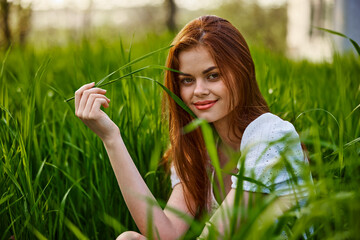 portrait of a cute red-haired woman sitting in tall grass and holding a leaf in her hands