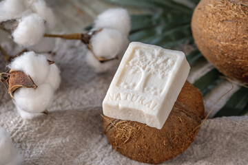 A piece of white soap with the inscription Natural and the image of a tree, coconut and cotton on the table
