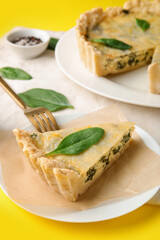 Plate with piece of delicious quiche on yellow background