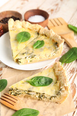 Plate with pieces of delicious quiche and spices on white wooden background