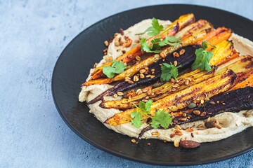 Multicolored baked carrots with hummus on black plate. Vegan recipe.