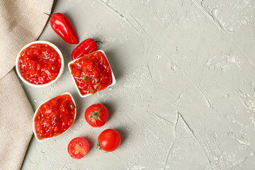 Composition with different bowls of delicious salsa sauce and ingredients on grey grunge background
