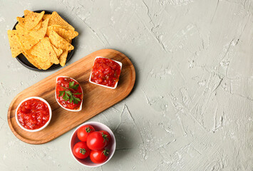Board with different bowls of delicious salsa sauce, nachos and tomatoes on grey grunge background