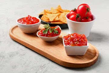 Board with different bowls of delicious salsa sauce on grey grunge background