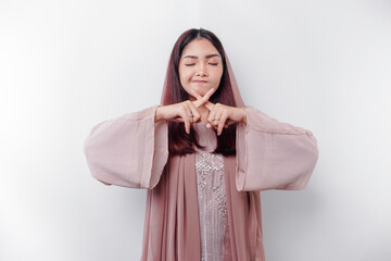 Beautiful Asian Muslim woman wearing a hijab with hand gesture pose rejection or prohibition with...