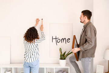Young couple hanging frame on light wall at home