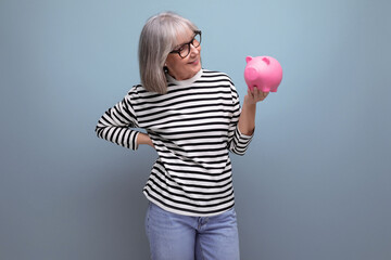 dreamy grandmother middle-aged woman holding a piggy bank with savings on a bright background with...
