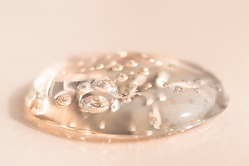 Drop of transparent face serum on a beige background, flat lay. Liquid transparent texture macro.