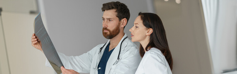 Two doctors in uniform look and discuss an X-ray or MRI scan of the patient spine