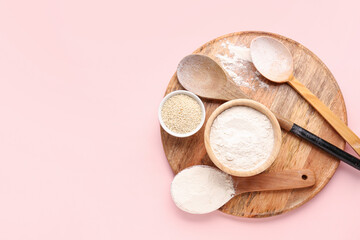 Board with bowl of wheat flour, sesame seeds and spoons on pink background