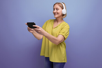 Fototapeta premium blonde 50s woman watching broadcast on smartphone using headphones
