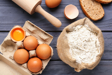 Composition with sack bag of wheat flour, eggs, bread and rolling pin on blue wooden table