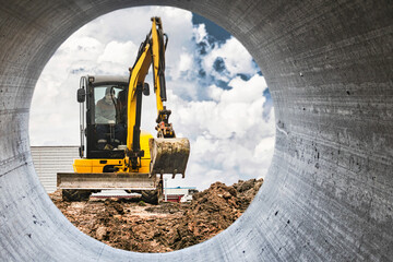 Mini excavator at the construction site on the edge of a pit against a cloudy blue sky. Compact...