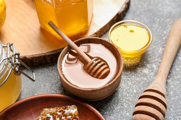 Bowl of sweet honey with dipper on grey background