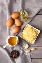 Bowl with tasty mayonnaise sauce and ingredients on grey wooden background