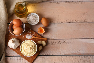 Fototapeta na wymiar Bowl with tasty mayonnaise sauce and ingredients on light wooden background