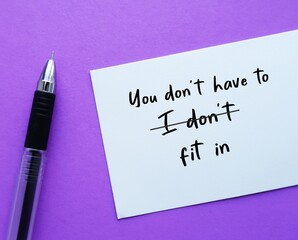 Pen on purple background with handwritten text on paper I DONT FIT IN, changed to YOU DONT HAVE TO FIT IN, to build self acceptance, stop needing others validation and be yourself