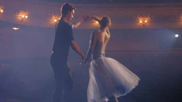 Beautiful ballet dancers practice and rehearse choreography on classic theater stage illuminated by spotlights. Man and woman prepare for theatrical dance performance. Art of classical ballet dance.