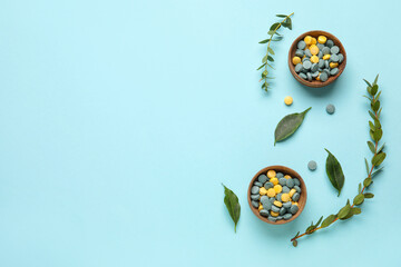 Bowls with pills and plant branches on blue background
