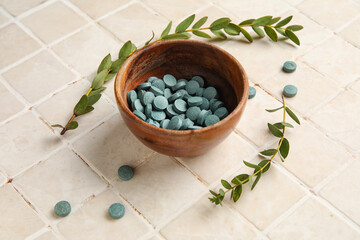 Bowl with pills and plant branches on beige tile background, closeup