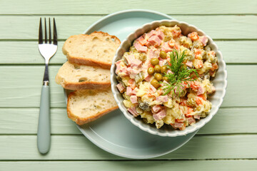 Bowl of tasty Olivier salad and bread on green wooden background