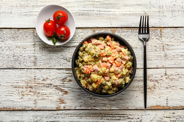 Bowl of tasty Olivier salad on light wooden background