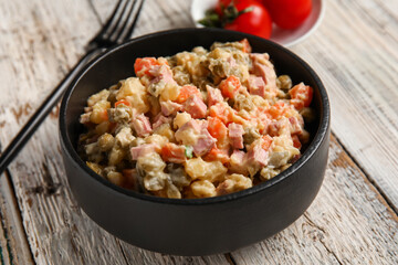 Bowl of tasty Olivier salad on light wooden background, closeup