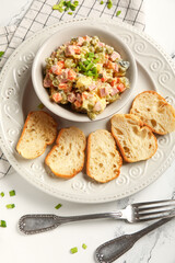 Bowl of tasty Olivier salad and bread on white marble background