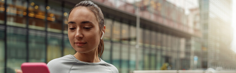 Obraz premium Young healthy sporty woman using cell phone during rest after jog. Blurred background