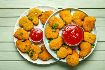Plates of tasty nuggets with ketchup on green wooden background