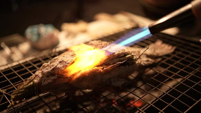 Sea bass or grouper fish grilled over charcoal. Close-up shot cooking seafish with aromatic spices on barbecue grill plate. Baking roasting marinated delicious seafood. BBQ in summer garden outdoors