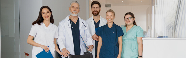 Group of professional doctors in uniform standing in clinic hall with medical wheelchair