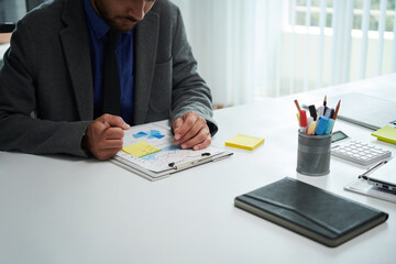 Serious entrepreneur analyzing chart and taking notes on yellow sticker