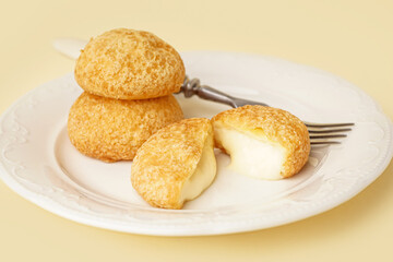 Plate with delicious choux pastry on beige background