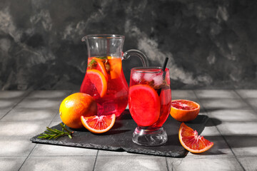 Glass and jug of tasty blood orange lemonade on dark background