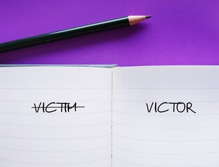 Notebook on purple background with handwriting VICTIM and VICTOR, to overcome victim mentality ( feels like have no control over things) develop attitude or behavior to change or  improve position