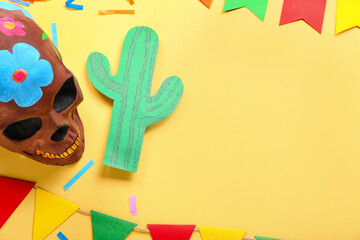 Painted skull with paper cactus, confetti and Mexican flags on yellow background