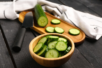 Bowl with fresh cut cucumber on dark wooden background
