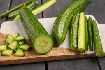 Board with fresh cut cucumbers on dark wooden background, closeup