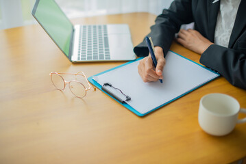Hands jotting down important information in documents and laptop with copy space and coffee cup...