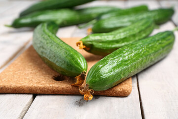 Board with fresh cucumber on light wooden background, closeup